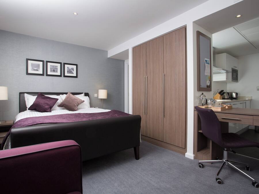 A modern hotel room with a bed, desk, chair, and wardrobe.
