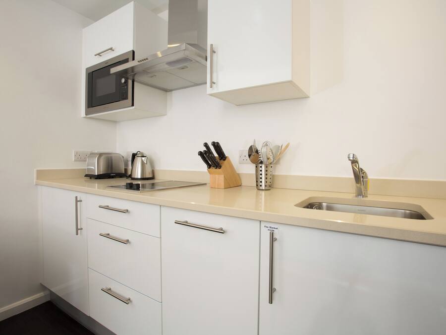 A modern kitchen with white cabinetry, a stainless steel sink, a kettle, and a knife block.
