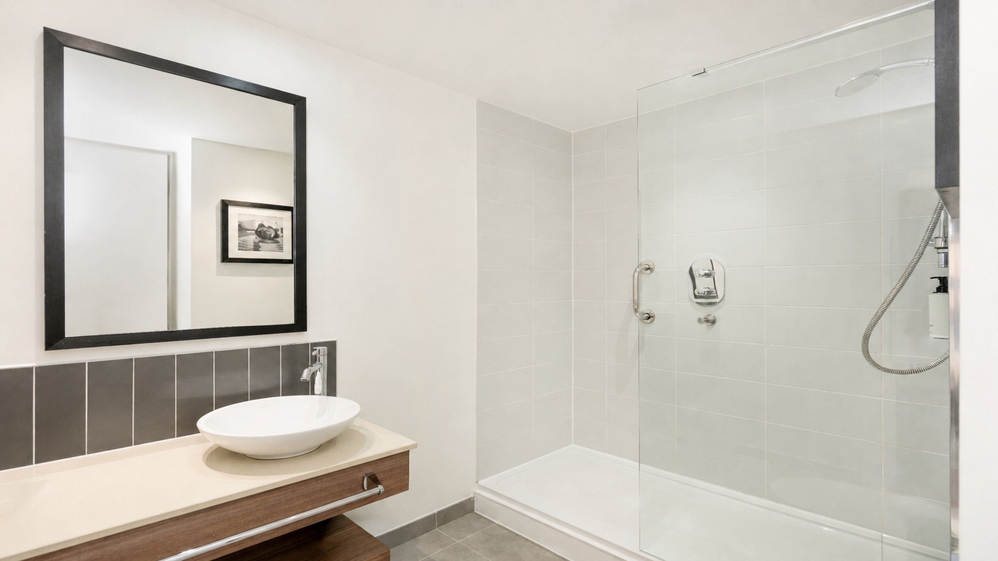 Un baño moderno con un espejo grande, un lavamanos y una ducha con mampara de vidrio.