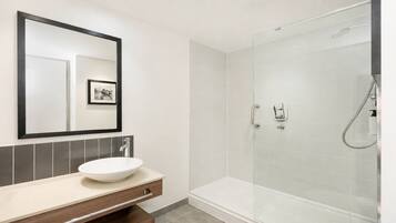 Un baño moderno con un espejo grande, un lavamanos y una ducha con mampara de vidrio.