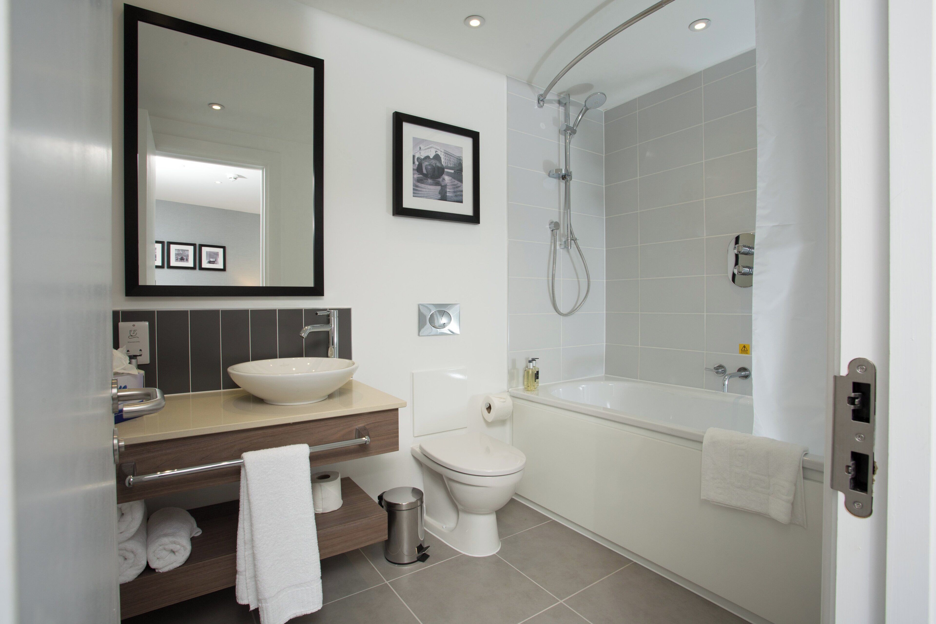 A modern bathroom with a large mirror, a sink, a toilet, and a bathtub.