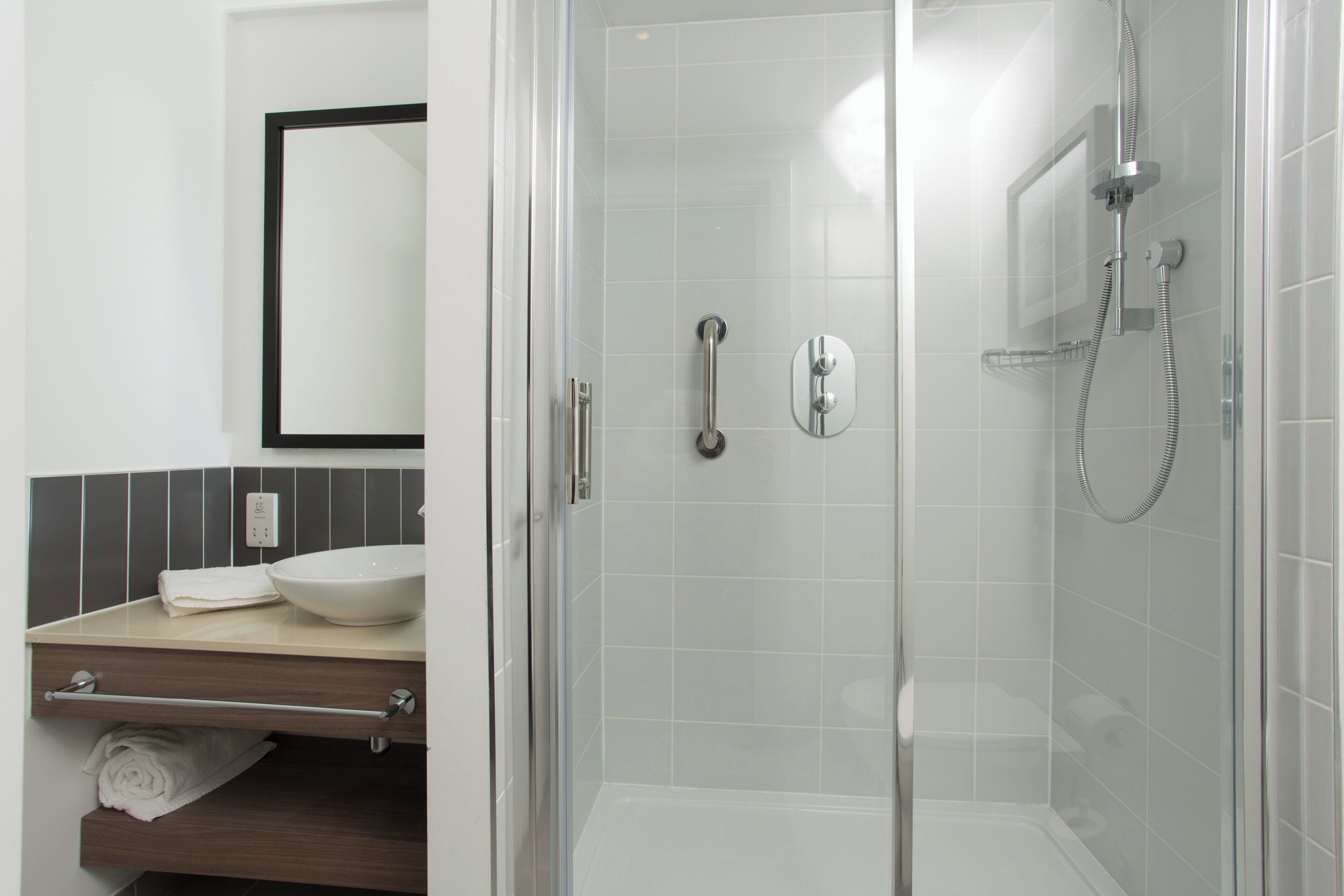 A modern bathroom with a glass-enclosed shower, a white sink, and a mirror above the countertop.