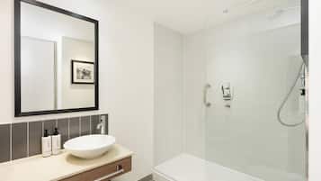 Un baño moderno con lavamanos, espejo y ducha blancos.