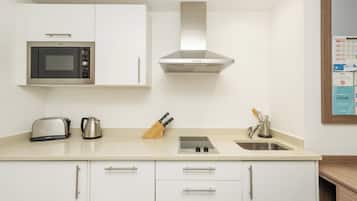 Una cocina moderna con armarios blancos, un microondas de acero inoxidable, un hervidor, un bloque de cuchillos y un fregadero.
