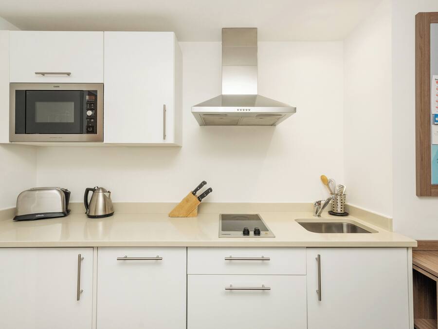 Una cocina moderna con armarios blancos, un microondas de acero inoxidable, un hervidor, un bloque de cuchillos y un fregadero.