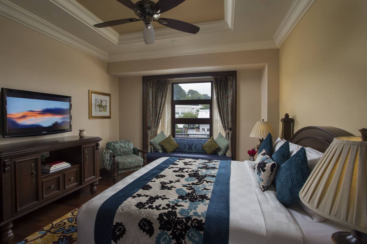 A hotel room with a bed, a television, a desk, and a window with curtains.