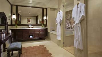 Une salle de bain spacieuse avec un grand miroir, un meuble-lavabo à deux vasques, une baignoire et deux peignoirs blancs suspendus à des crochets.