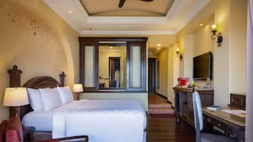 A hotel room with a large bed, a desk with a chair, a TV, and a ceiling fan.