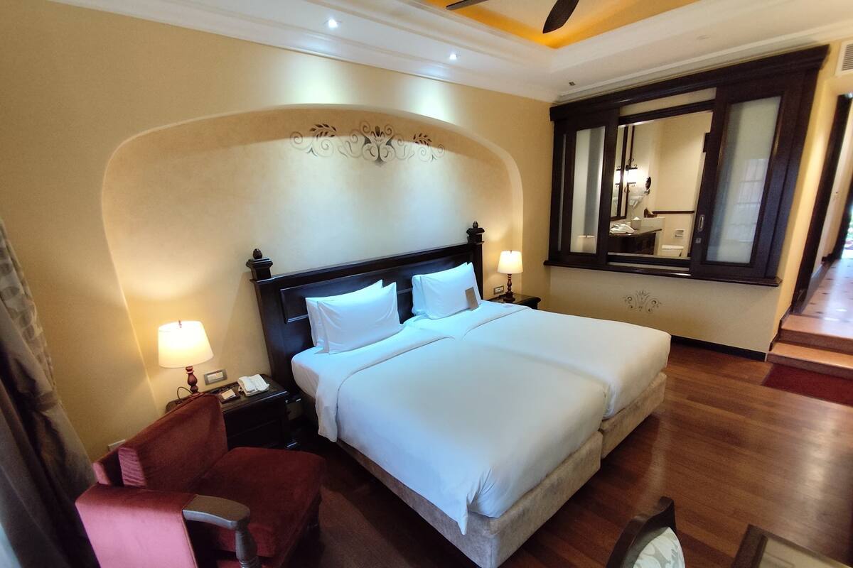 A hotel room with a large bed, a chair, a nightstand with a lamp, and a mirror.