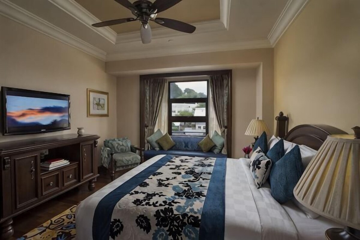 Habitación de hotel con cama, televisión, escritorio y ventana con cortinas.
