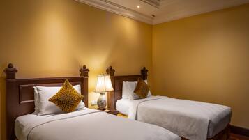 A hotel room with two beds, each with white bedding and a wooden headboard. There is a nightstand with a lamp between the beds.