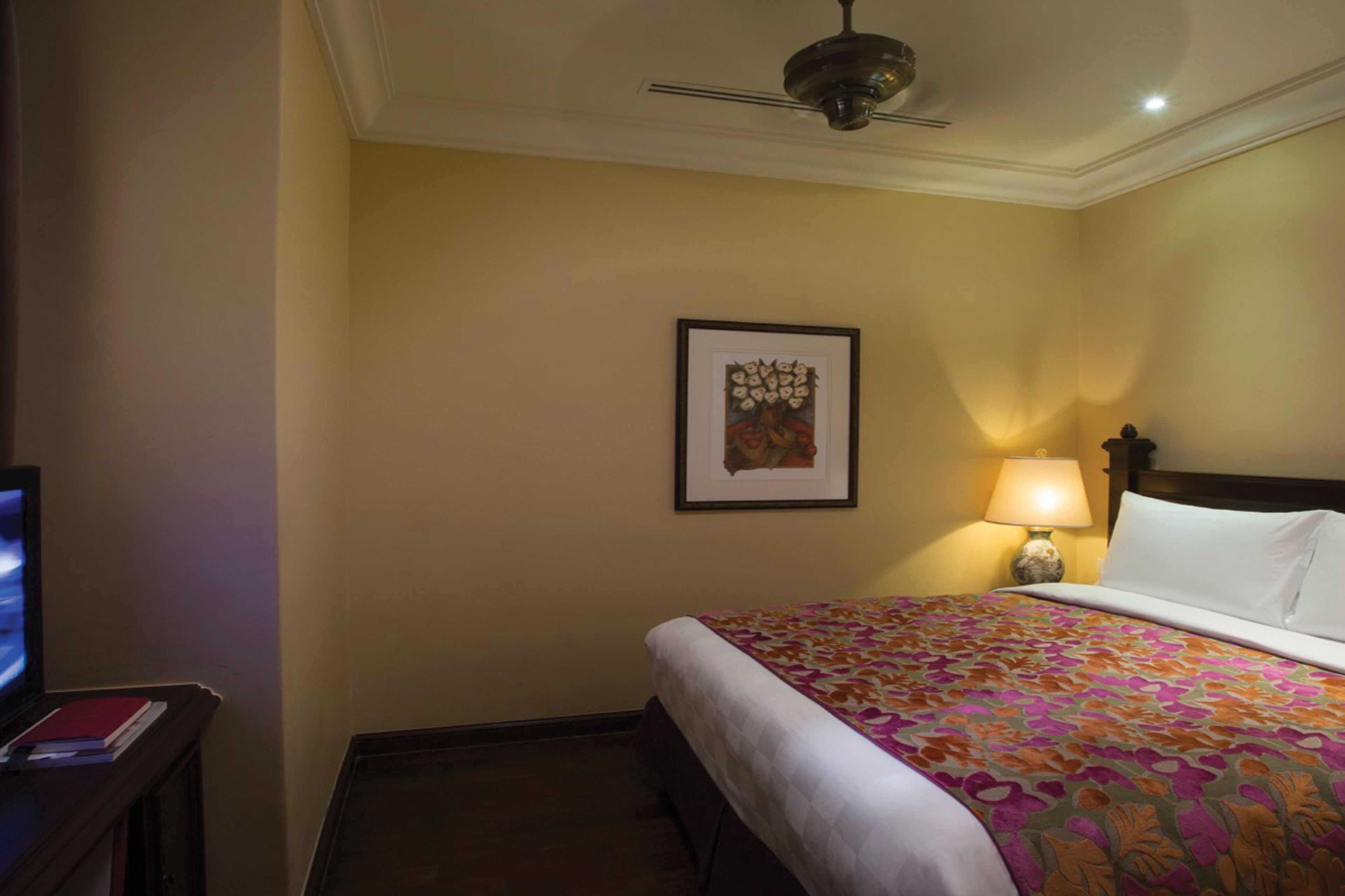 A hotel room with a bed, a television, a framed artwork on the wall, and a lamp.