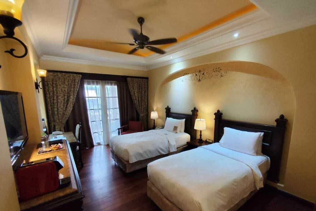 A hotel room with two beds, a desk with a chair, a television, and a ceiling fan.