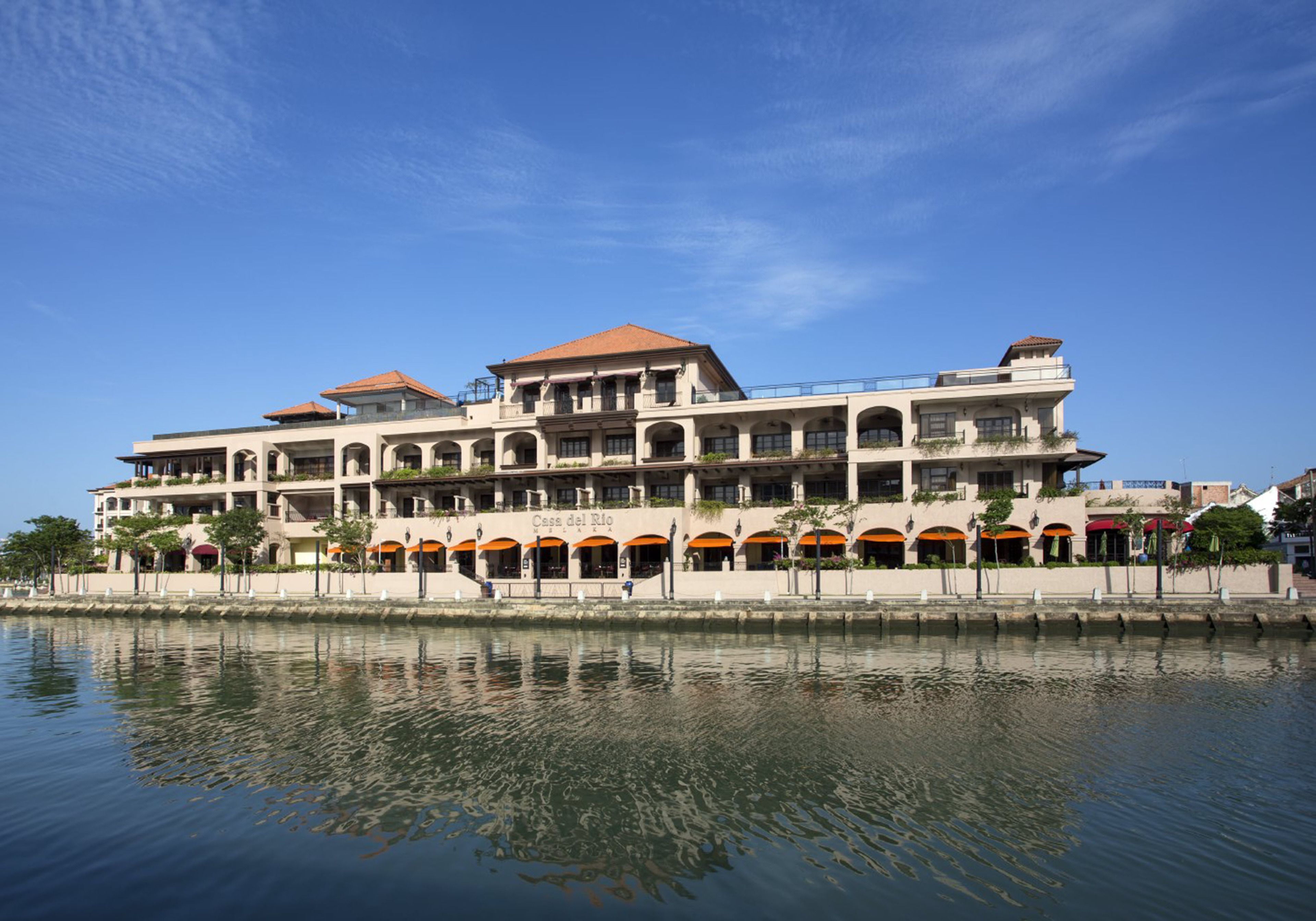 A large, multi-story hotel with a waterfront view, featuring a series of balconies and outdoor seating areas.