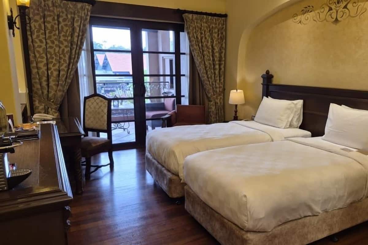 A hotel room with two beds, a desk, a chair, and a balcony with a view.