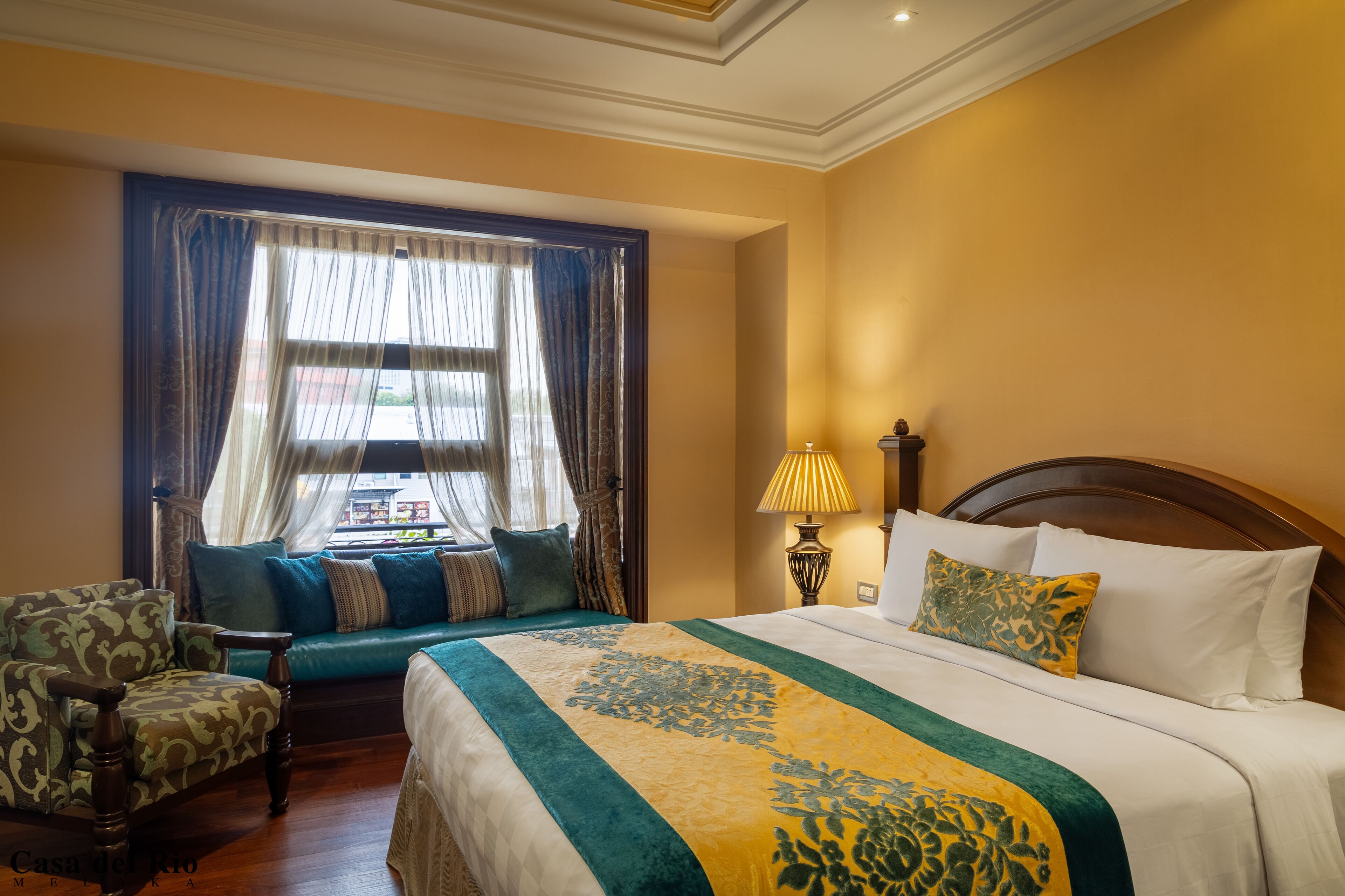 A hotel room with a large bed, a sofa, a chair, and a window with curtains.