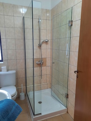 A glass-enclosed shower stall with a toilet and a blue towel on the floor. - Marinea Villas (Chlorakas)