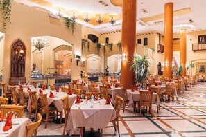 A spacious dining area with multiple tables and chairs, large columns, and decorative plants. - Nubian Island Hotel (Sharm El Sheikh)