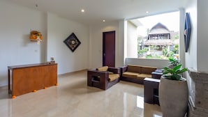 A spacious living area with a wooden reception desk, a sofa set, a large potted plant, and a view of traditional architecture outside. - Villa Sonia Bisma (Ubud)