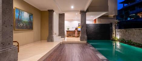 A modern hotel lobby with a wooden floor, a pool, and a painting on the wall.