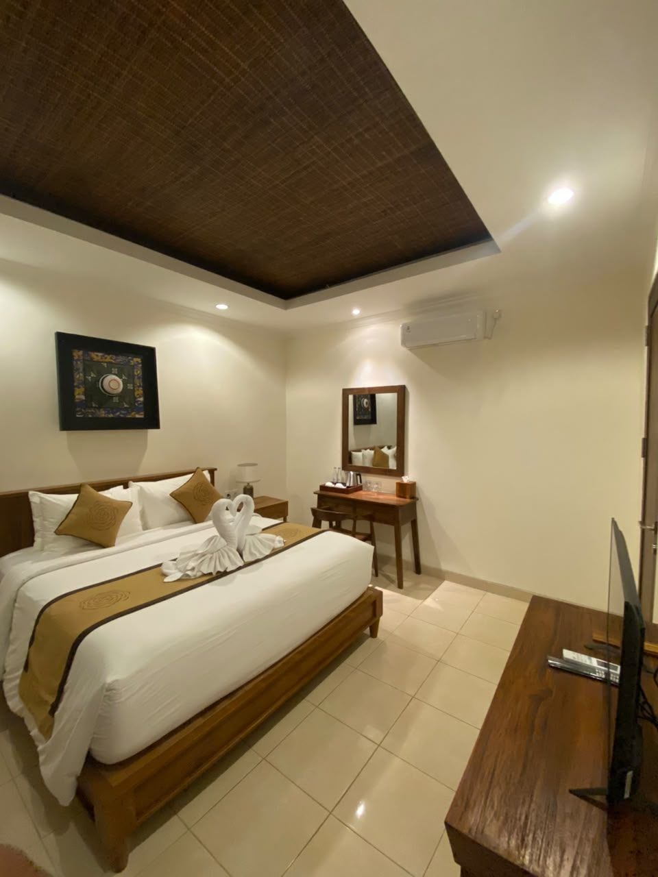 A hotel room with a large bed, a wooden desk, a mirror, and a television.