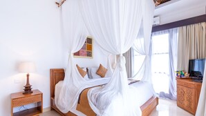 A neatly arranged bedroom with a four-poster bed, a bedside table with a lamp, and a television on a wooden cabinet. - Villa Sonia Bisma (Ubud)