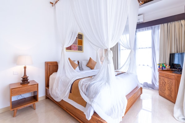 A neatly arranged bedroom with a four-poster bed, a bedside table with a lamp, and a television on a wooden cabinet. - Villa Sonia Bisma (Ubud)
