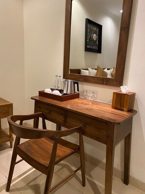 A wooden desk with a chair, a mirror, a framed picture, and a tray with bottles and a kettle. - Villa Sonia Bisma (Ubud)