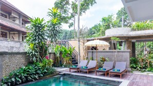 A pool area with lounge chairs and a stone wall. - Villa Sonia Bisma (Ubud)