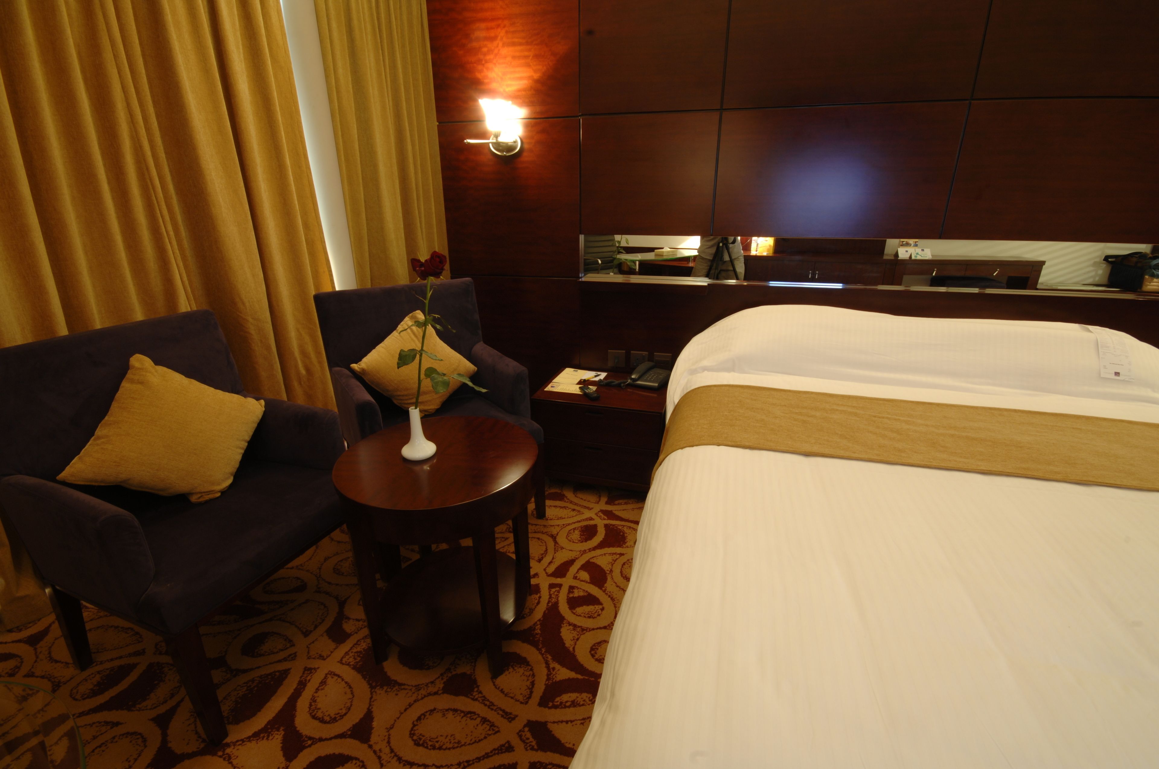 Een hotelkamer met een bed, twee fauteuils, een tafeltje met een vaas en een spiegel aan de muur.