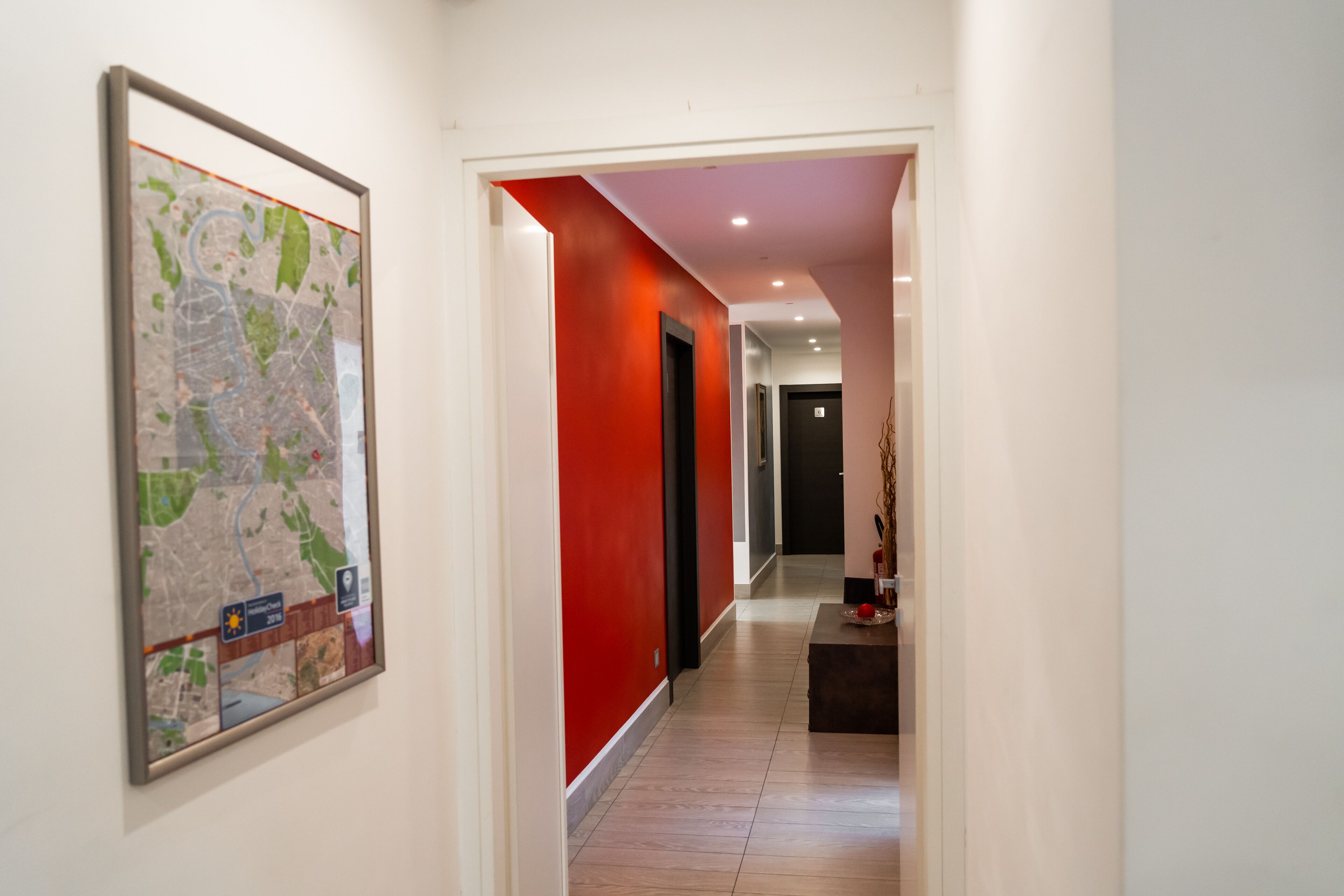 A hallway with a red accent wall, a framed map, and a dark door at the end.
