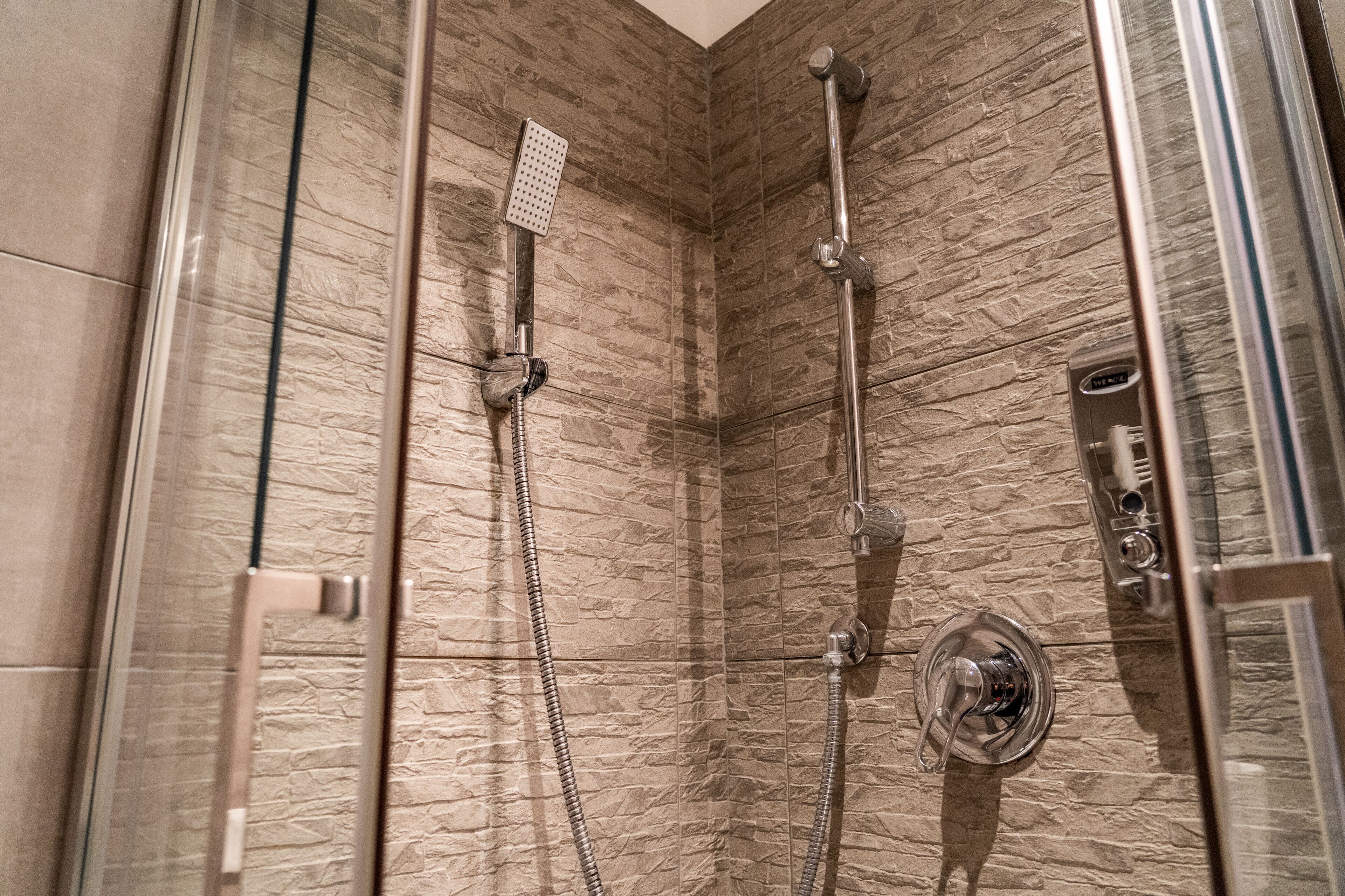 A modern shower with a glass door, a handheld showerhead, a wall-mounted faucet, and a control panel.