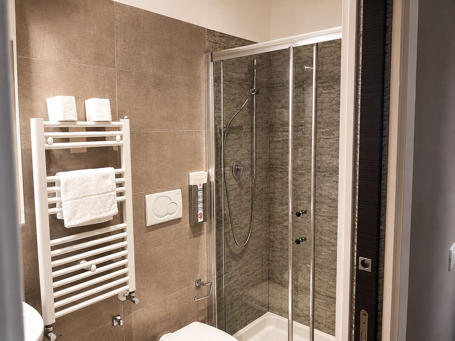 A modern bathroom with a glass-enclosed shower, a white towel rack, and a control panel.