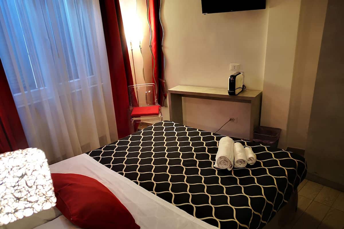 A hotel room with a bed, a desk, a chair, and a TV mounted on the wall.