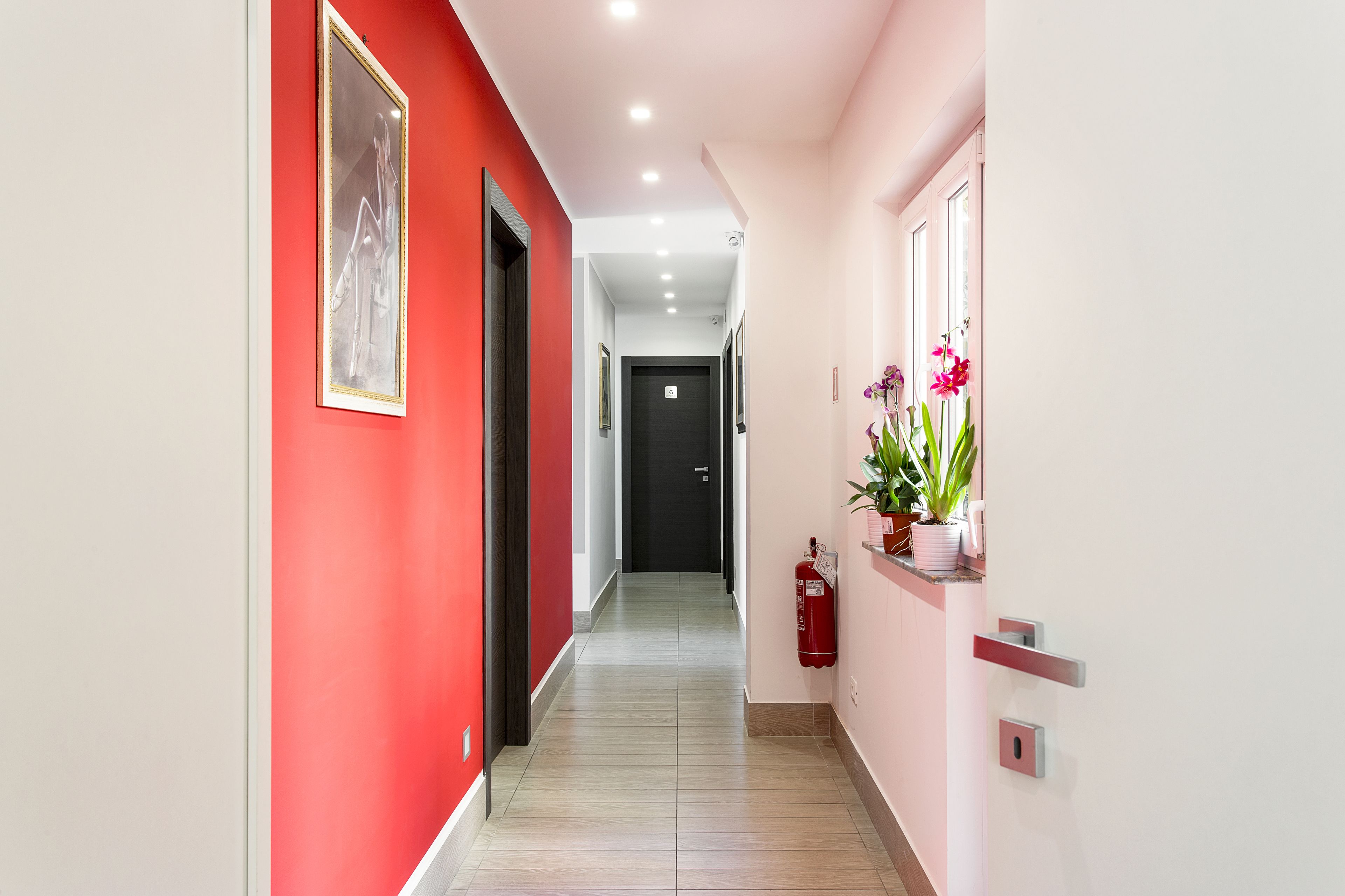 A hallway with a red wall, a black door at the end, and a fire extinguisher on the right.