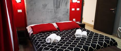 Une chambre d’hôtel avec un lit, des oreillers rouges, une tête de lit grise et un téléviseur fixé au mur.
