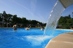 A swimming pool with a water slide and people playing in the water.