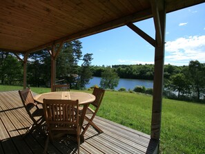 A wooden deck with a round table and chairs, overlooking a lake and surrounded by trees.