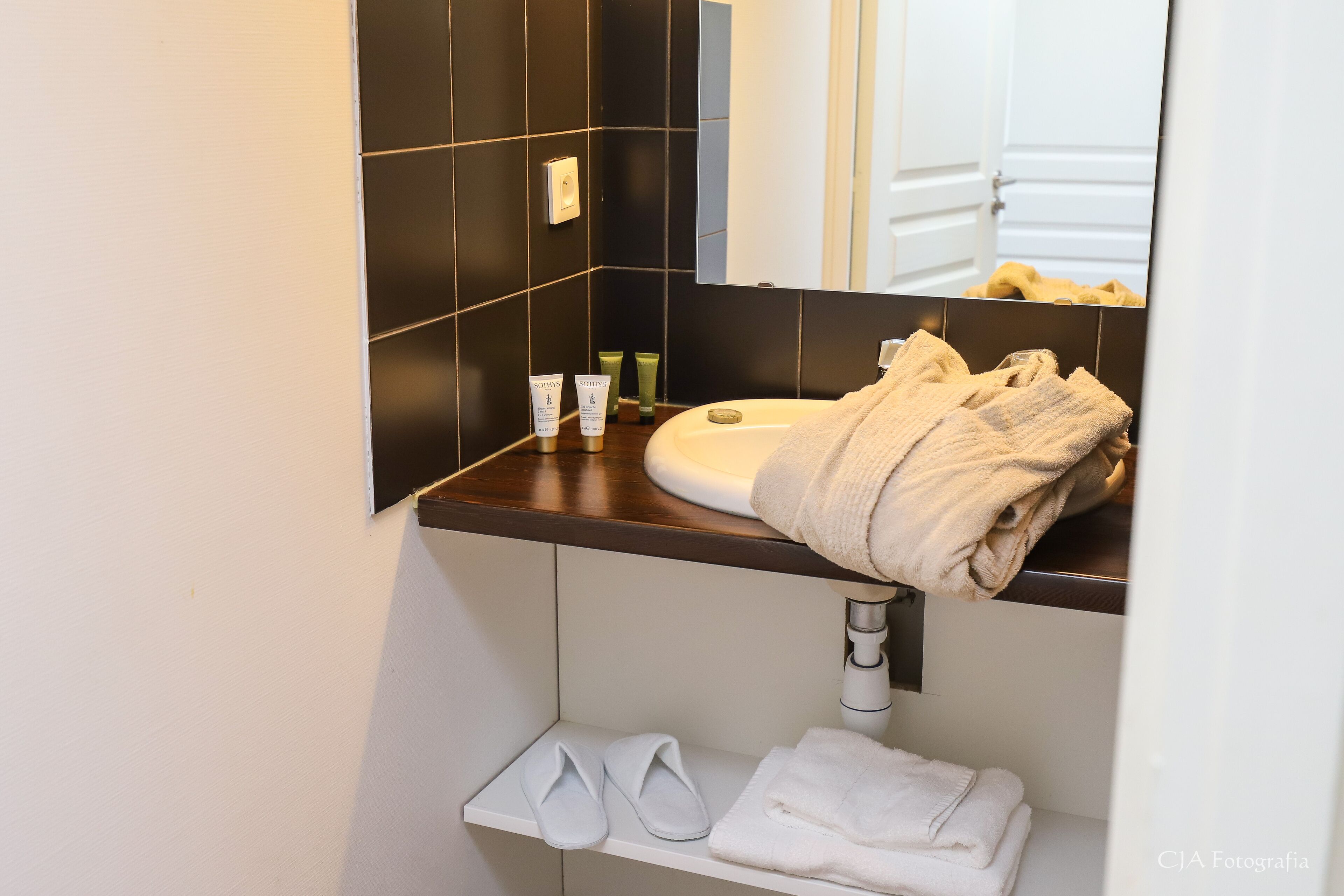 A bathroom with a white sink, black tiles, a mirror, and a towel rack.