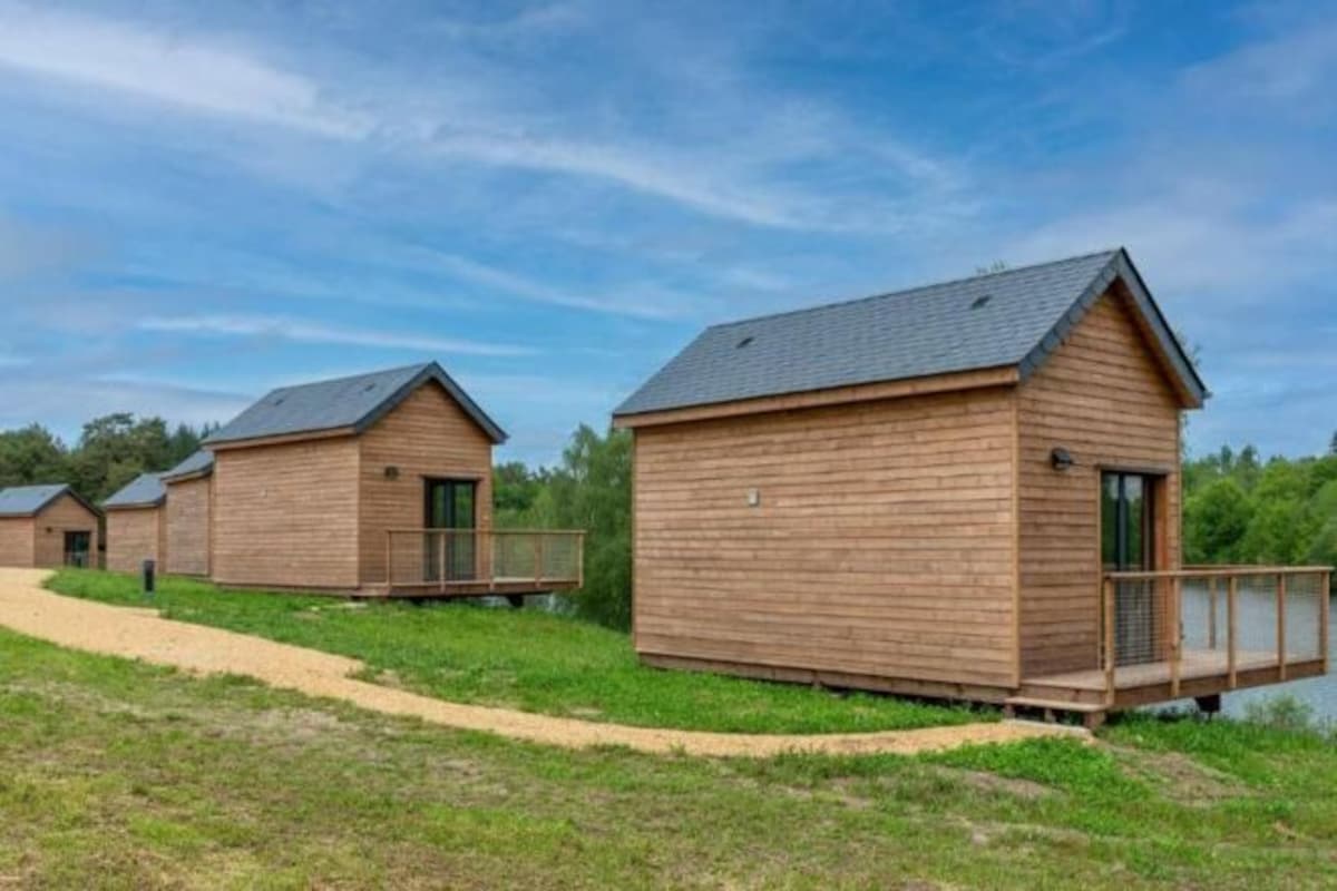 Una hilera de cabañas de madera con terraza, un sendero y una masa de agua al fondo.