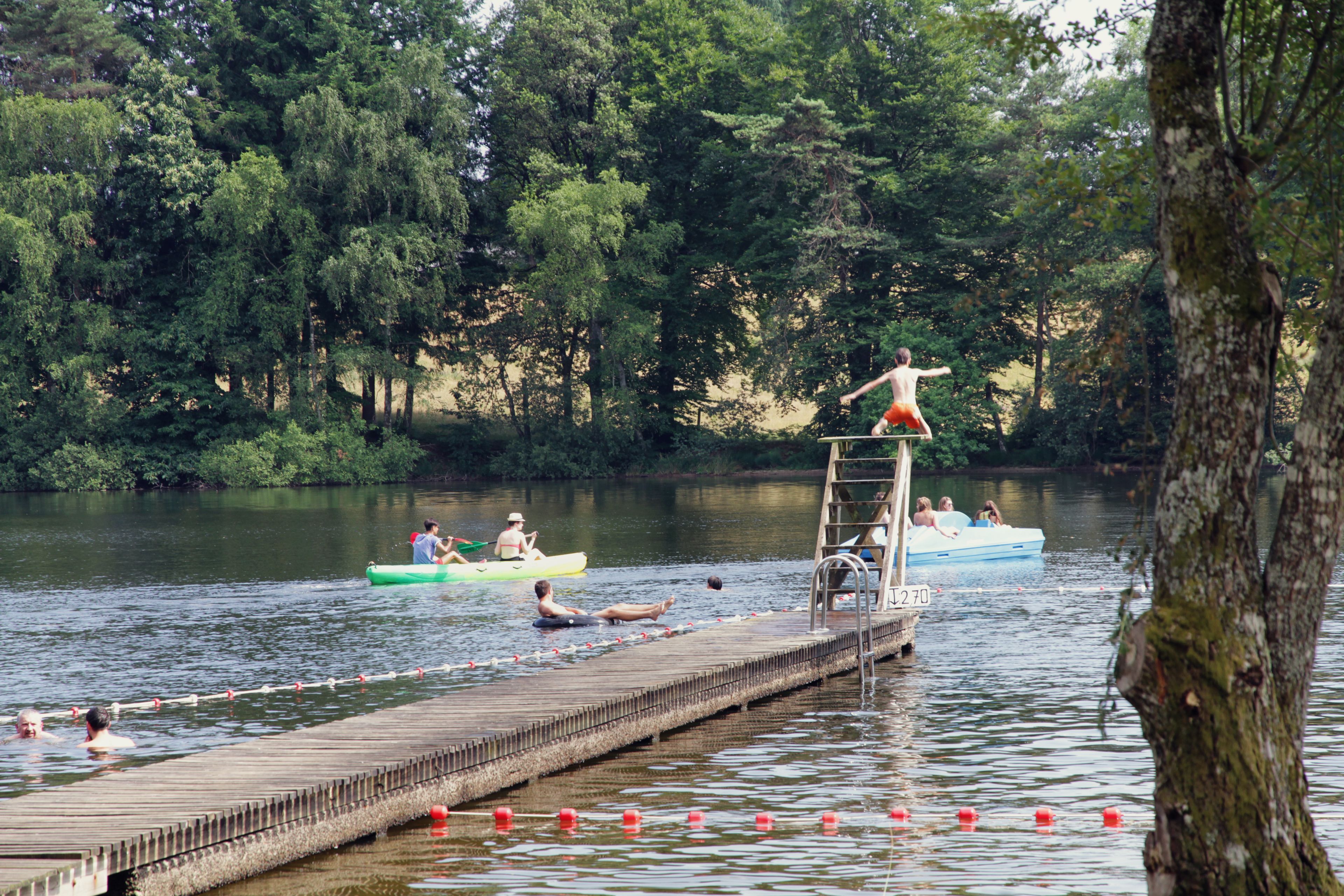 Eine hölzerne Mole, die in einen See hineinreicht, mit Menschen in Kanus und einer Leiter, die zu einem kleinen Boot führt.