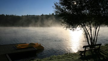 A serene lakeside scene with a dock, a yellow inflatable boat, and a bench under a tree.