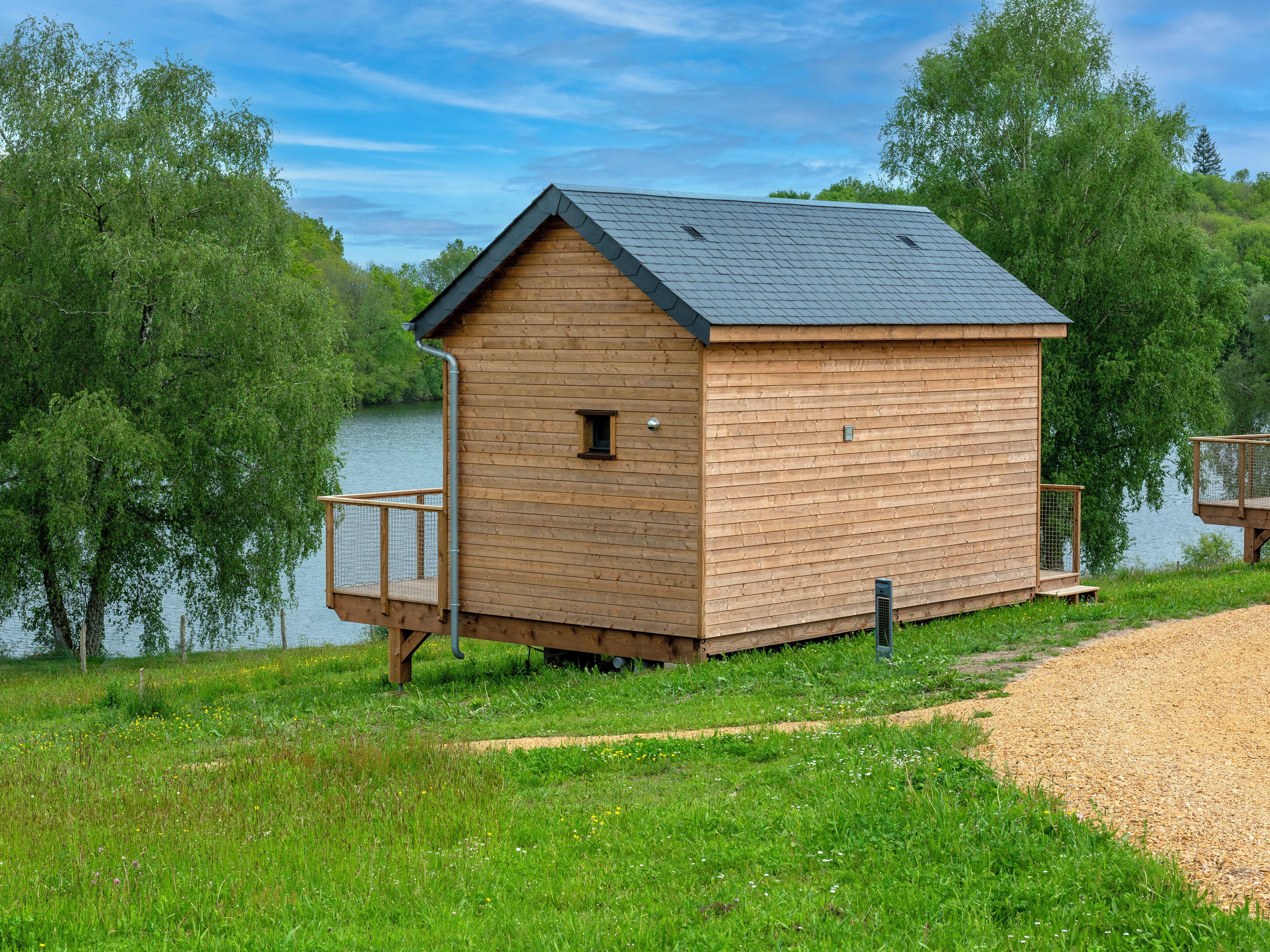 Een houten chalet met balkon, aan een meer gelegen, omringd door groen.