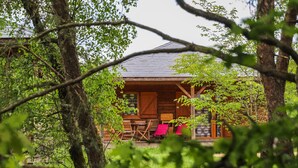 A wooden cabin with a porch, surrounded by trees.