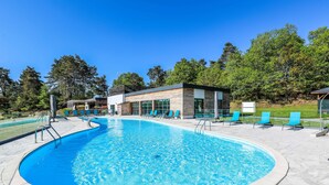 A swimming pool with a curved edge, surrounded by lounge chairs and a building with large windows.