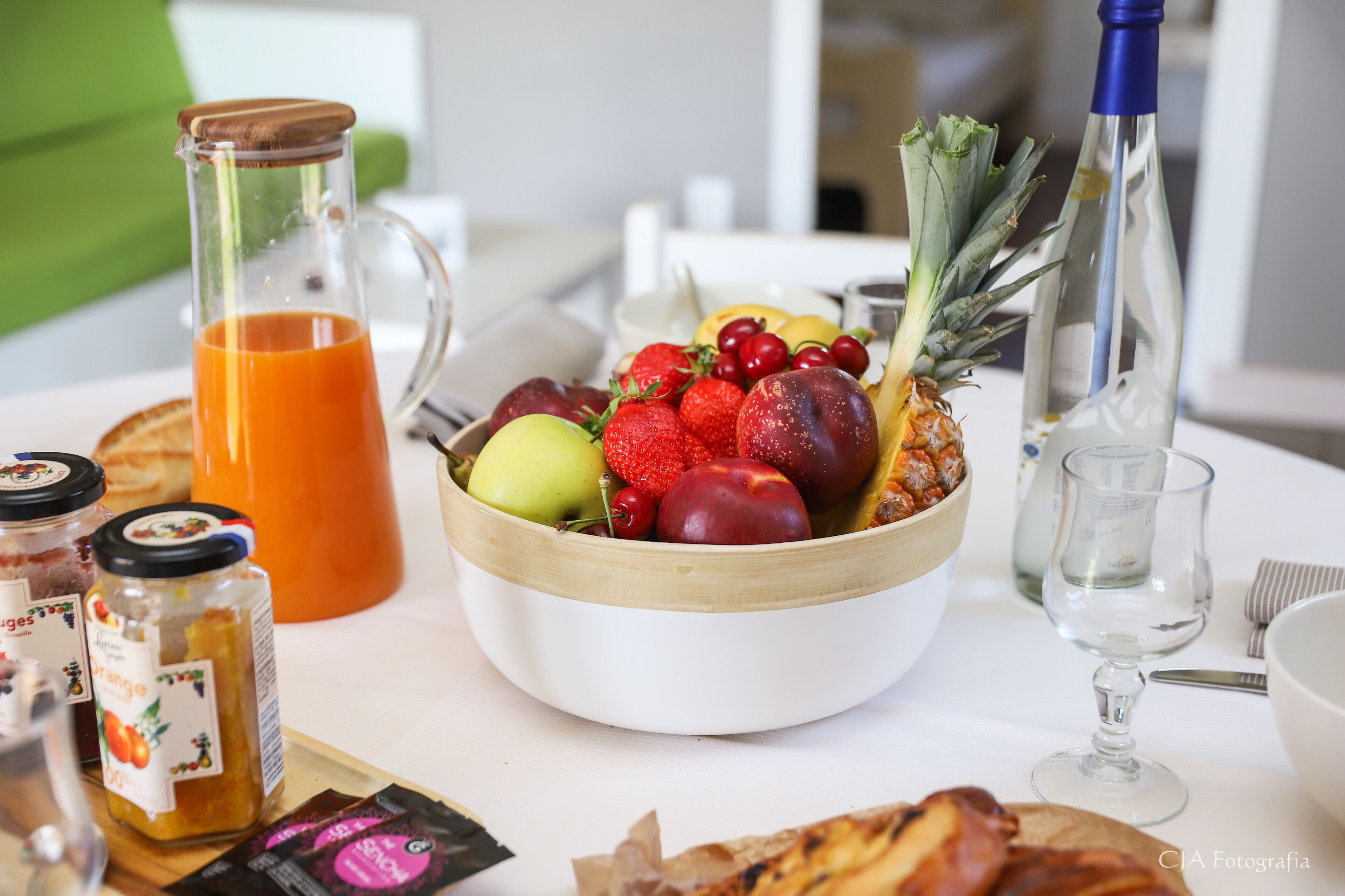 Ein Frühstückstisch mit Obstschale, Krug Orangensaft, Flasche und Glas.