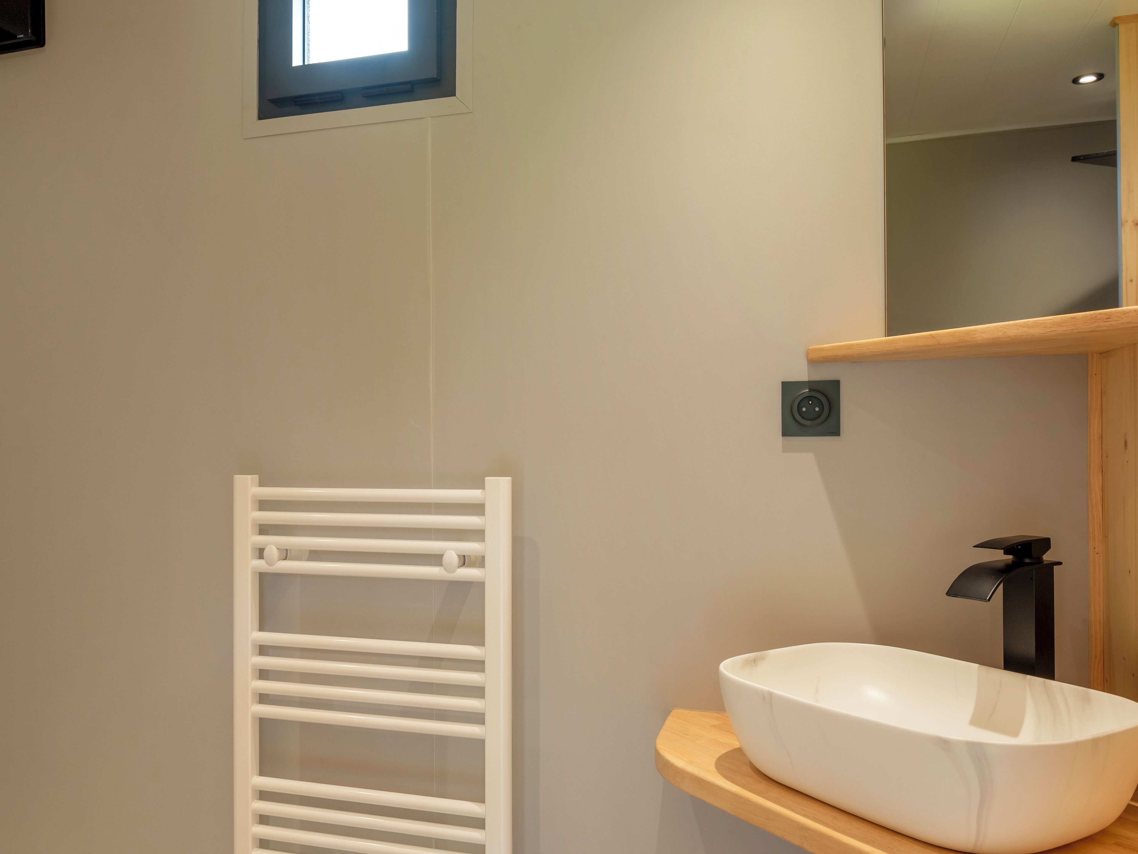 Casa de banho moderna com uma lavatório branco em cima de uma bancada de madeira, um porta-toalhas branco e uma pequena janela sobre a lavatório.