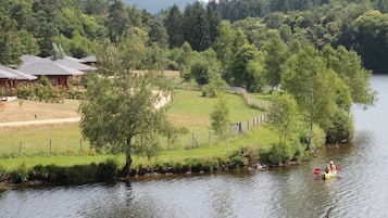 A lakeside cabin with a dock, surrounded by lush greenery and a forested backdrop.