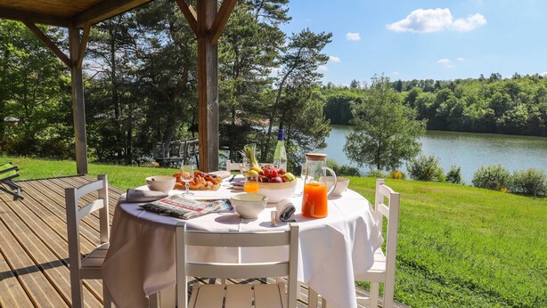 A table set for breakfast on a wooden deck with a lake view.