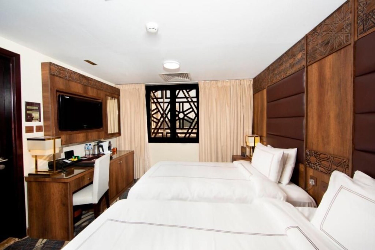 A hotel room with a large bed, a desk with a computer, a TV, and a decorative window.